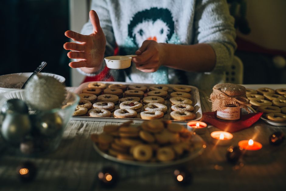 Hands dusting powdered sugar over freshly baked holiday cookies in a cozy kitchen setting