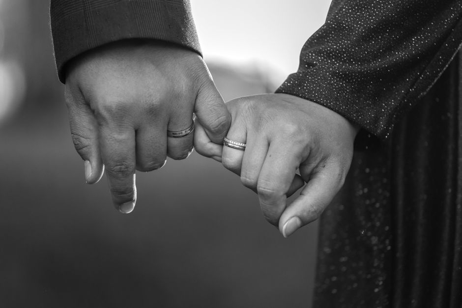 Close-up black and white photo of couple holding hands, engagement ring visible, symbolizing commitment